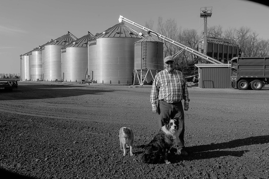Kevin Skunes with his dogs, Jack and Ike, in front of bins full of corn.